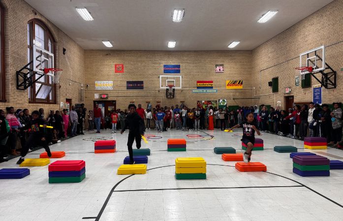  4 Clark students competing in relay race, as student spectators watch on